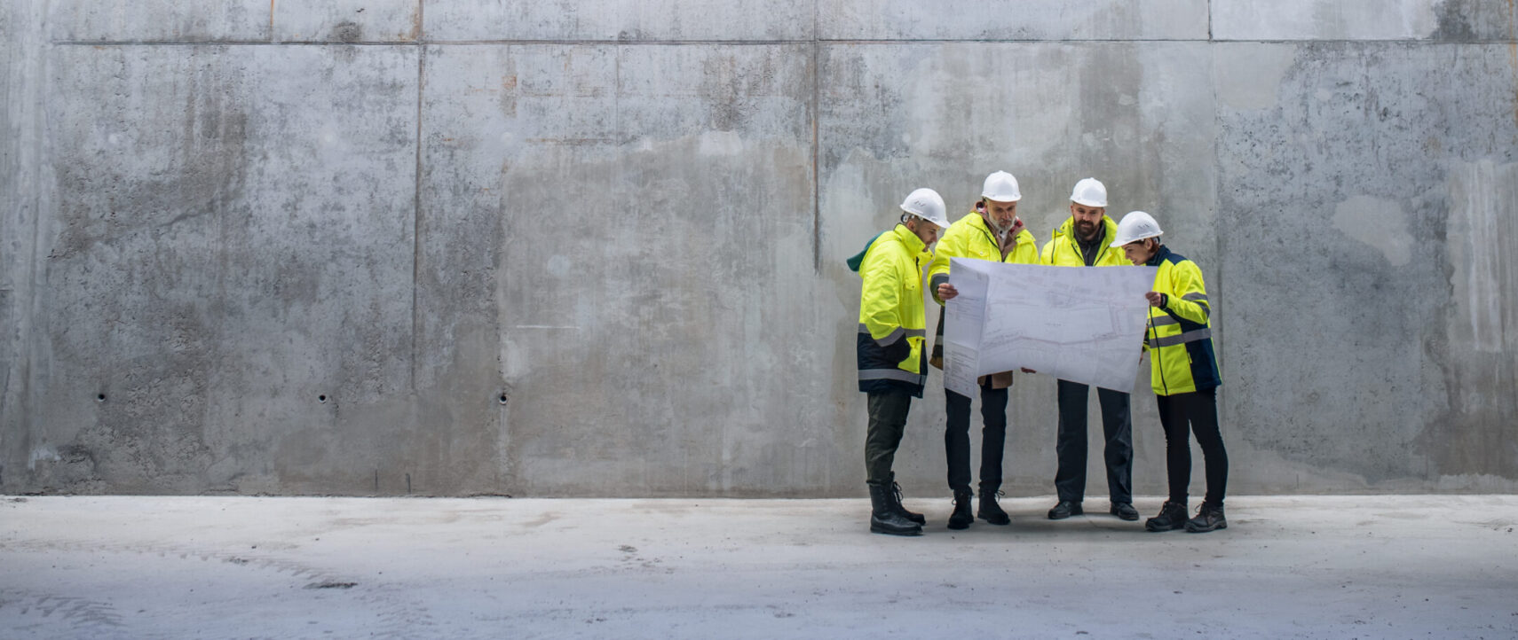 A Group Of Engineers Standing Against Concrete Wall On Construction Site.